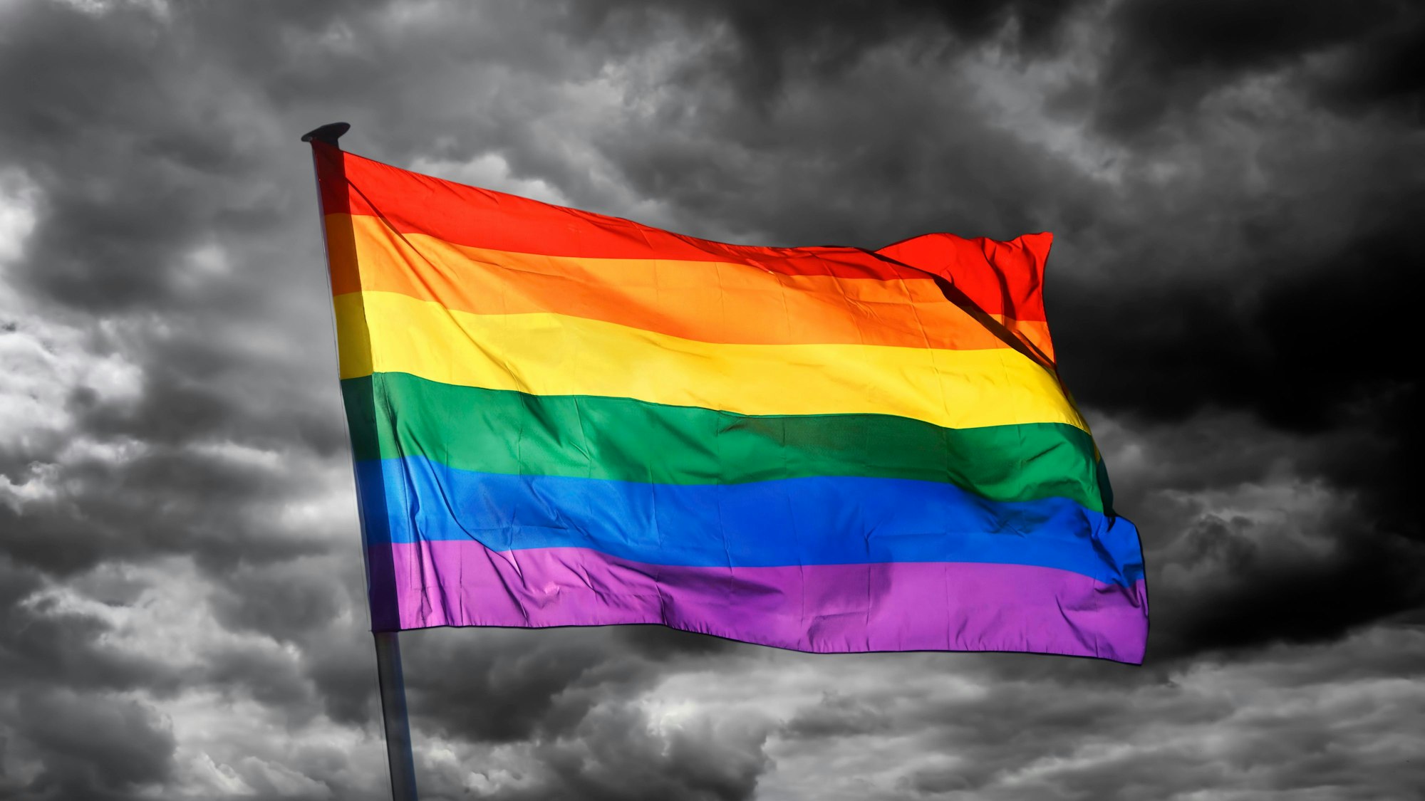 Wehende Regenbogenflagge vor dunklem Himmel