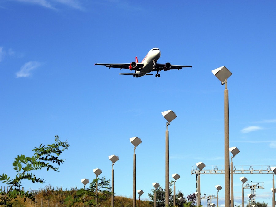 Flugzeug im Landeanflug über Lichtmasten und Vegetation