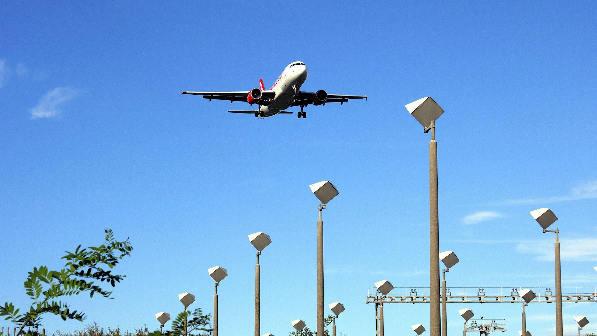Flugzeug im Landeanflug über Lichtmasten und Vegetation