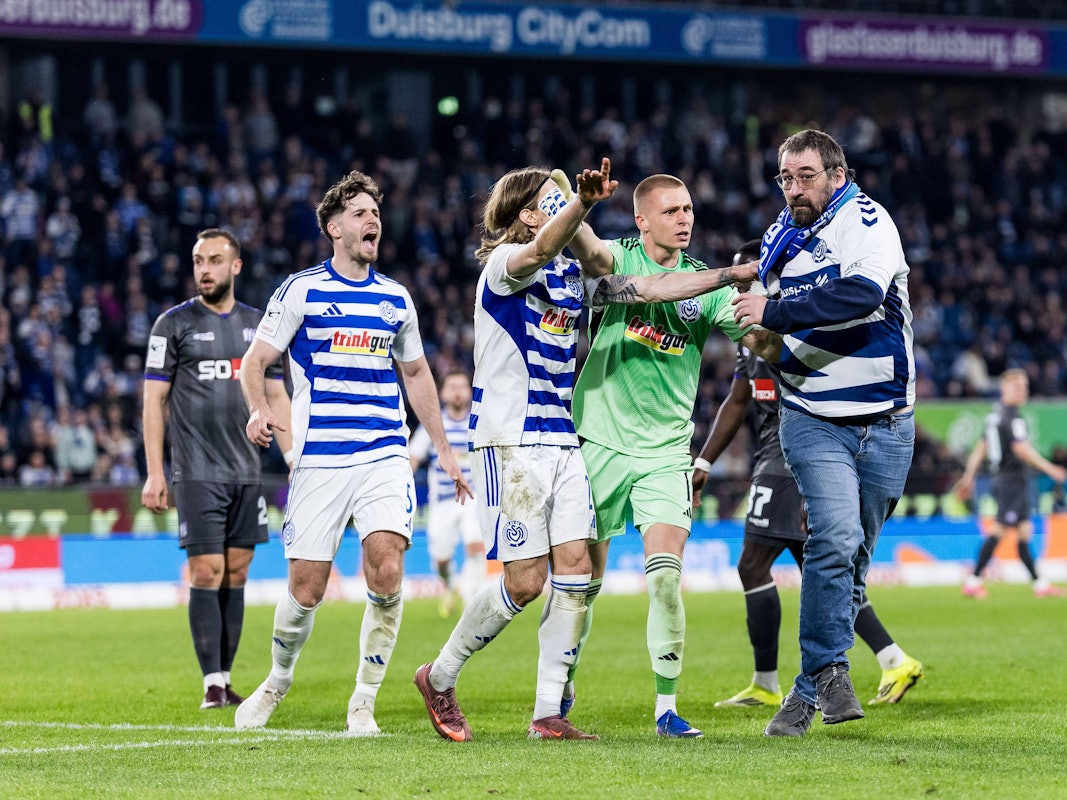 Ein Fan des MSV Duisburg wird von den Profis vom Feld geschoben.