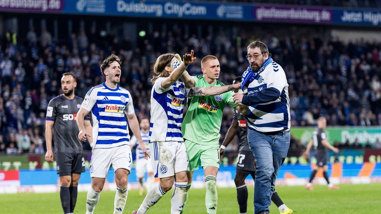 Ein Fan des MSV Duisburg wird von den Profis vom Feld geschoben.