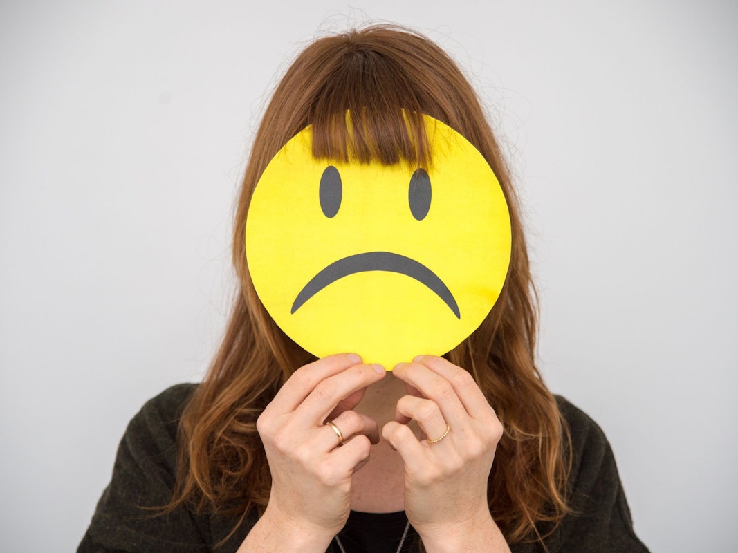 Eine Frau hält sich ein trauriges Smiley vor ihr Gesicht