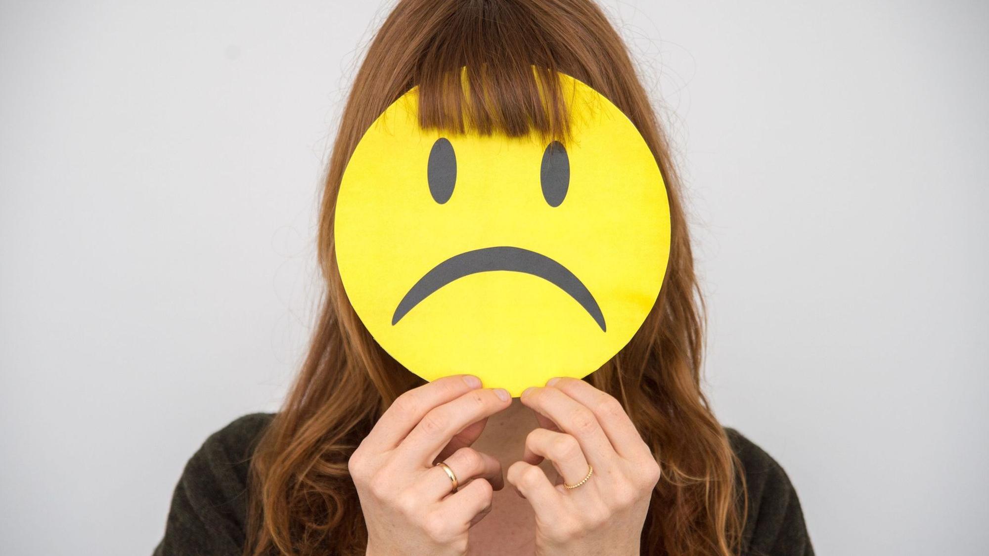 Eine Frau hält sich ein trauriges Smiley vor ihr Gesicht