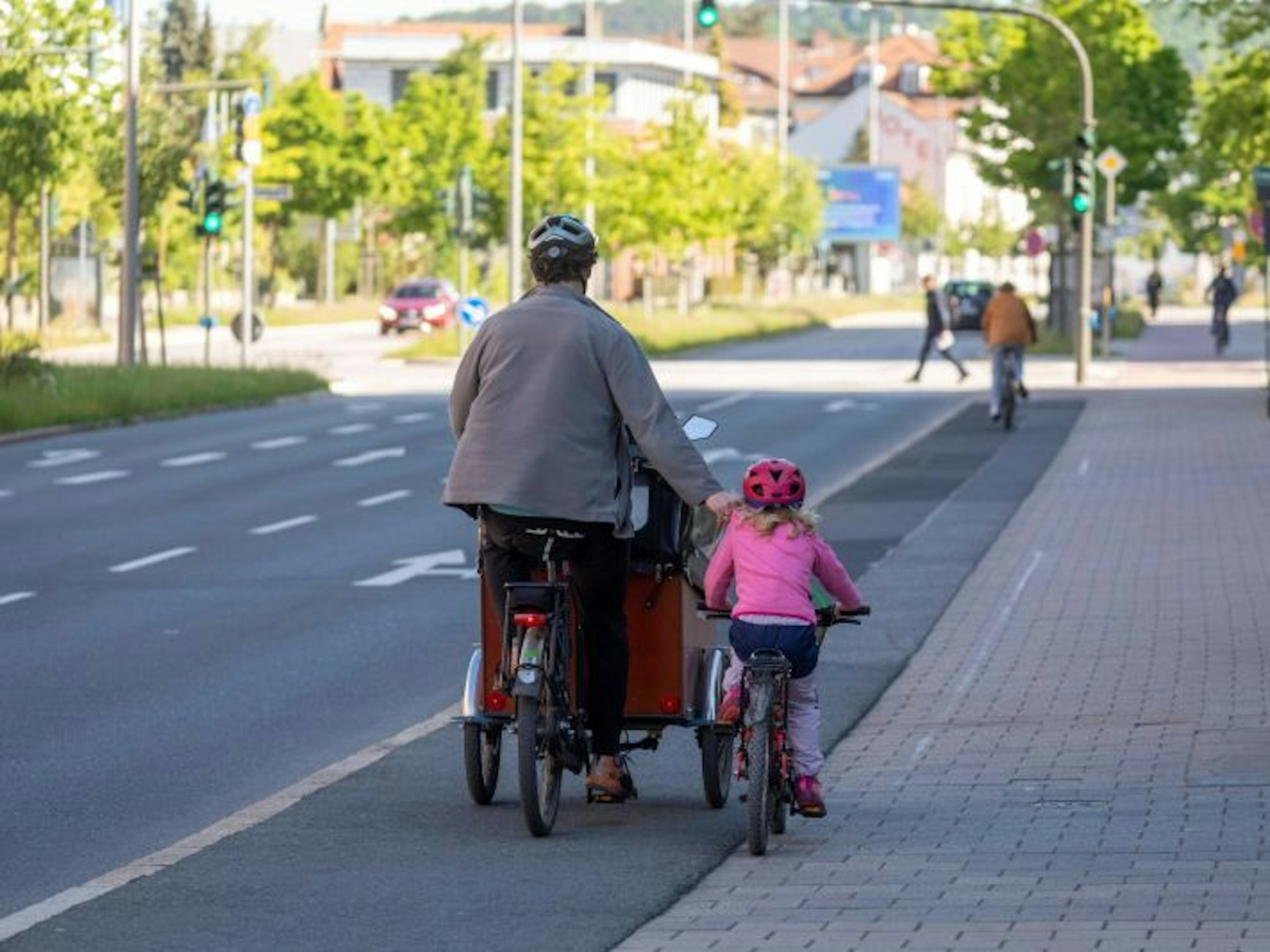 Das Symbolfoto zeigt einen Vater auf einem Lastenrad neben einem Kindr auf dem eigenen Kinderrad.