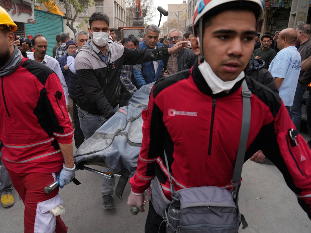 Mehrere Personen tragen eine Bahre, auf der ein Leichensack liegt.