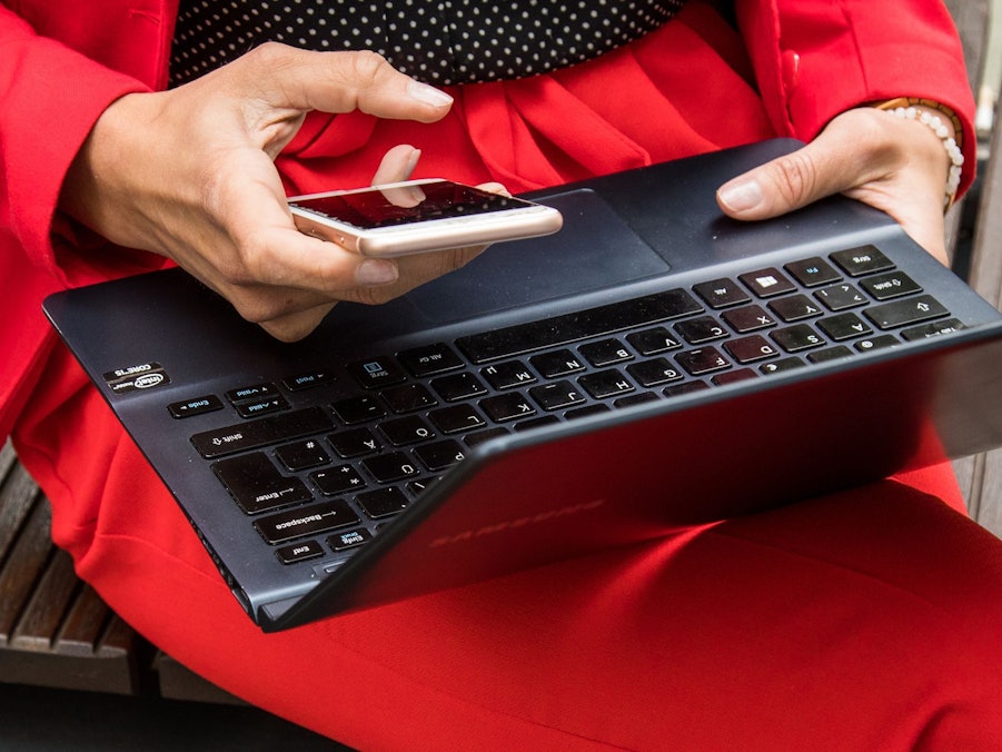 Eine Frau hält ein Smartphone und ein Laptop in den Händen