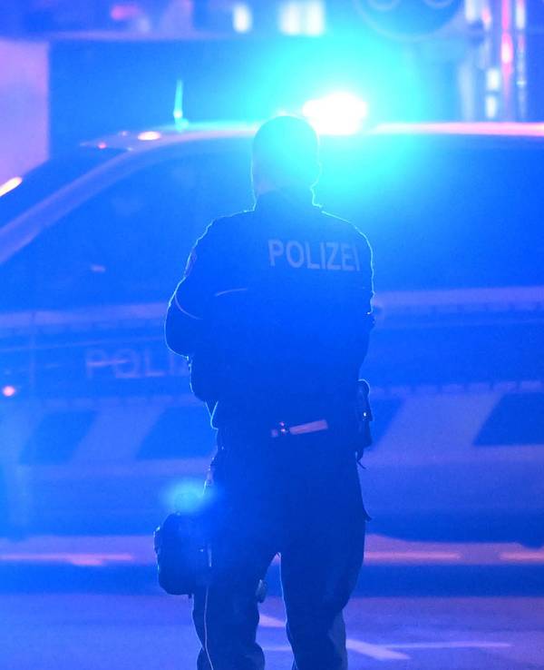 Ein Polizist steht vor einem Polizeifahrzeug, bei dem das Blaulicht eingeschaltet ist.