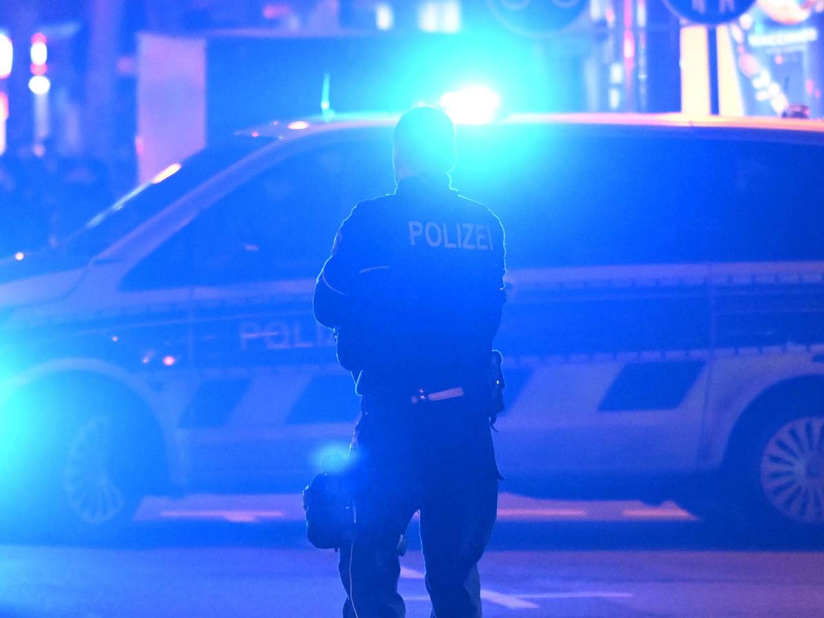 Ein Polizist steht vor einem Polizeifahrzeug, bei dem das Blaulicht eingeschaltet ist.