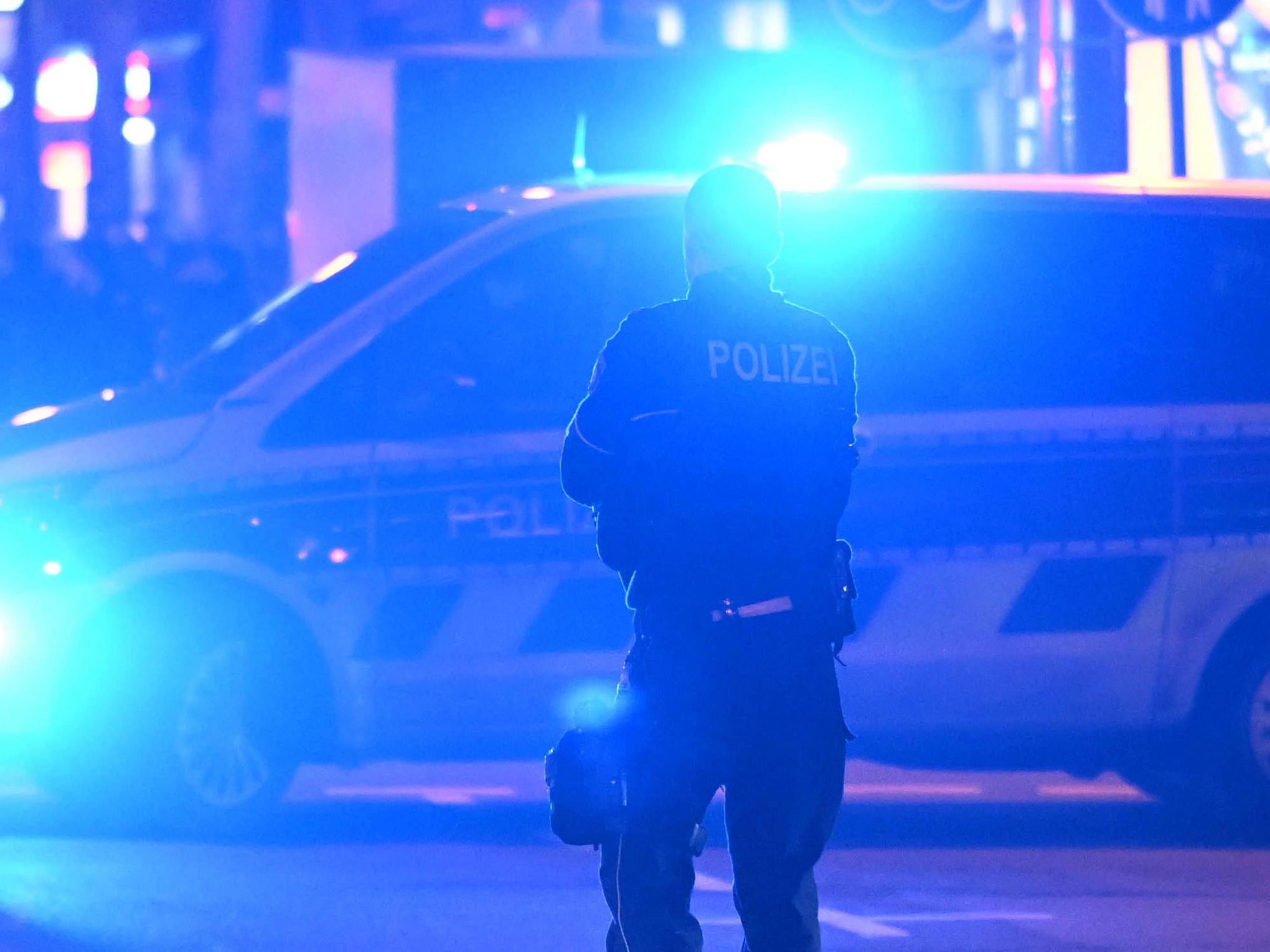 Ein Polizist steht vor einem Polizeifahrzeug, bei dem das Blaulicht eingeschaltet ist.