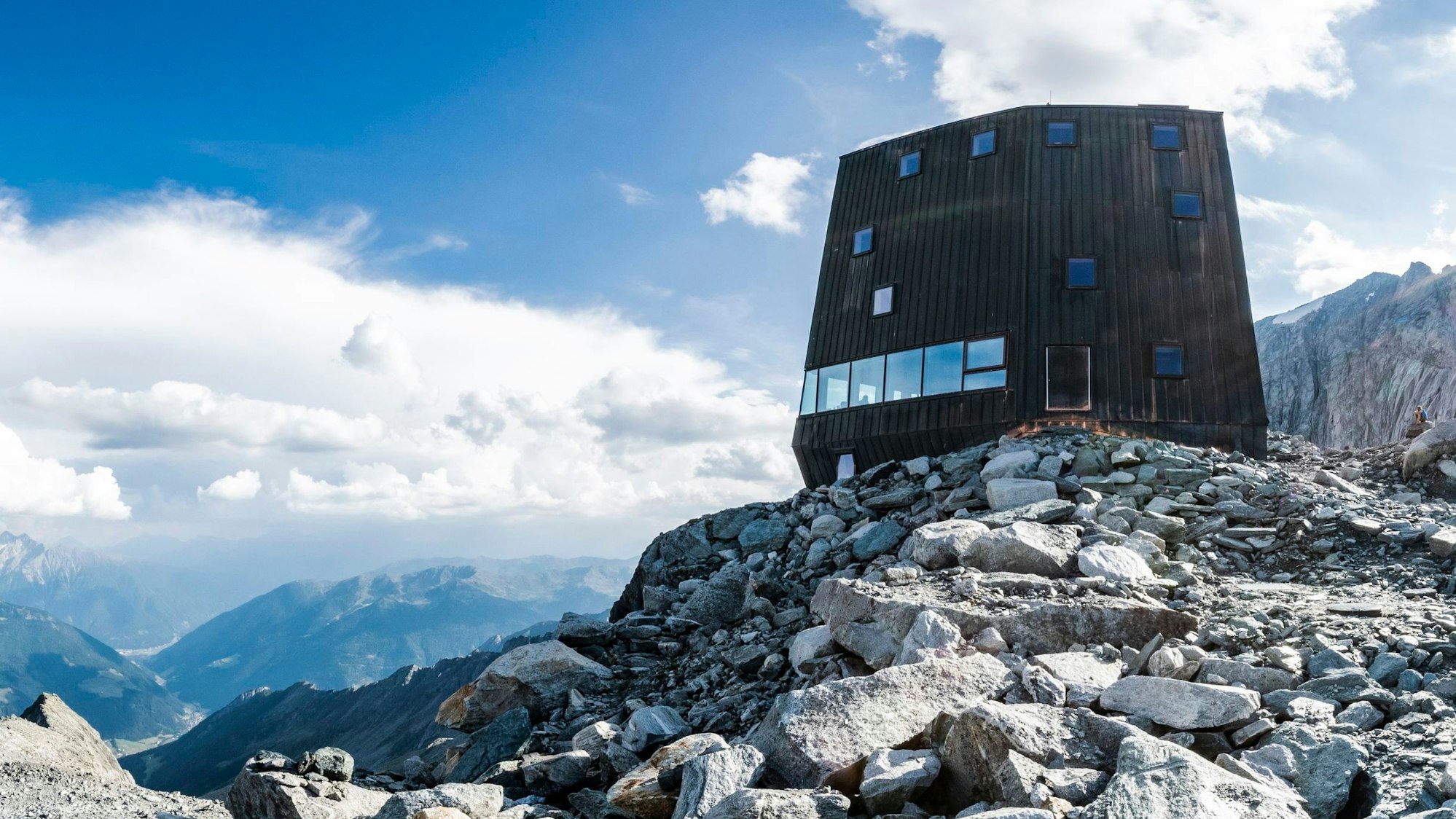 Eine Hütte die aussieht wie ein Bunker mit Schießscharten ragt auf kargen Felsen hoch auf einem Berggipfel empor.