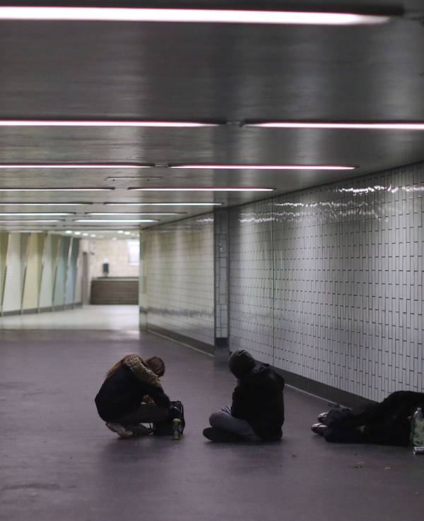 Eine Person liegt in einem Gang einer Haltestelle auf dem Boden, zwei weitere sitzen neben ihm.