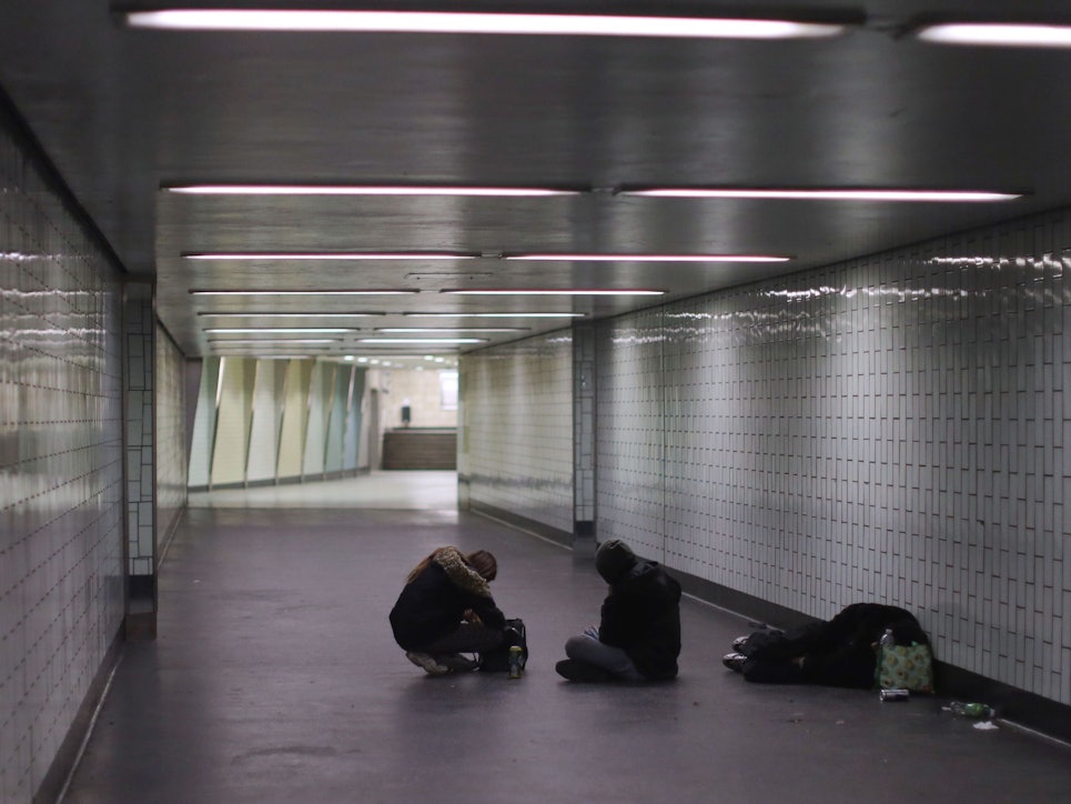 Eine Person liegt in einem Gang einer Haltestelle auf dem Boden, zwei weitere sitzen neben ihm.