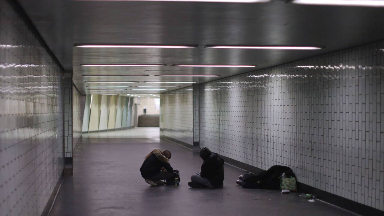 Eine Person liegt in einem Gang einer Haltestelle auf dem Boden, zwei weitere sitzen neben ihm.