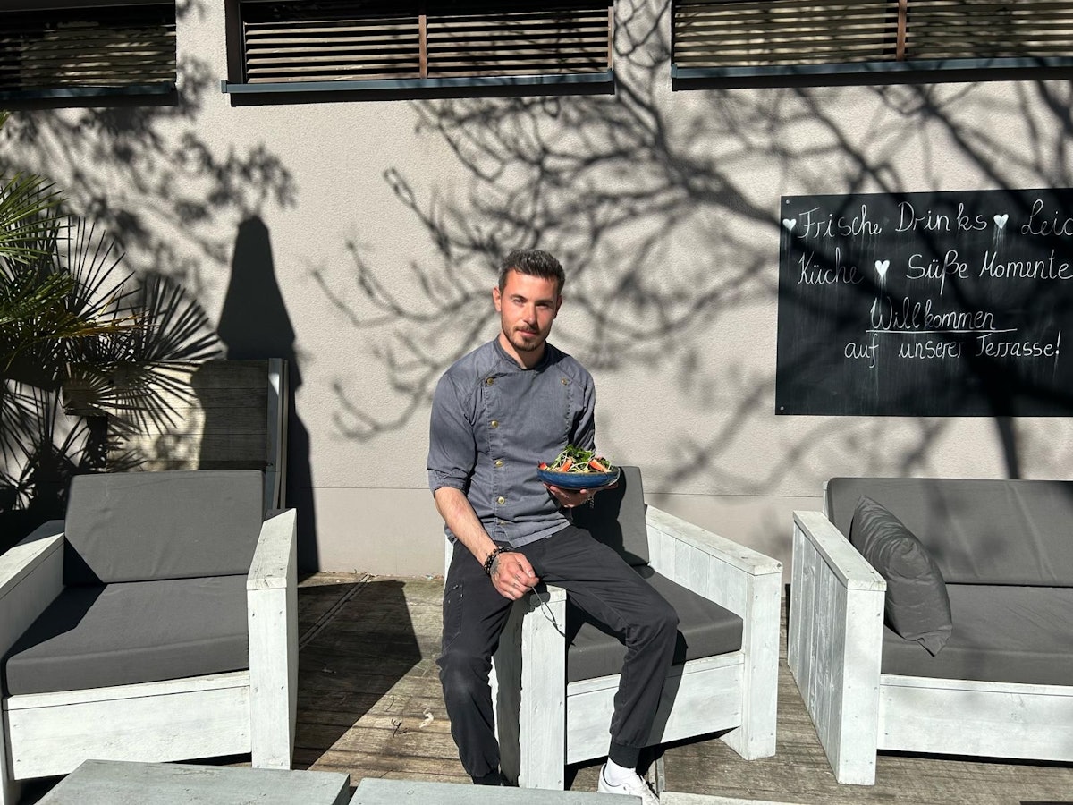 Ein Mann sitzt mit einem Teller Salat vor dem Sportcenter Kautz in Köln-Klettenberg.