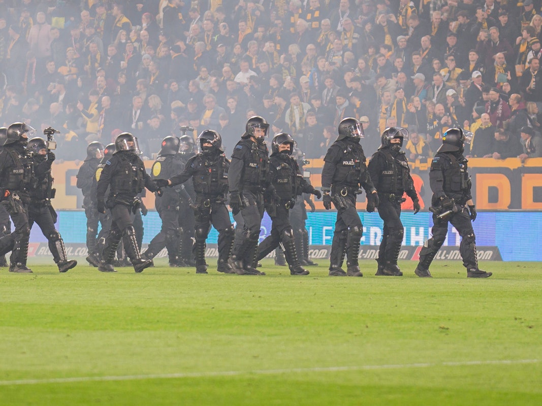 Beim Spiel von Dynamo Dresden stehen Polizisten in Einsatzmontur auf dem Rasen.