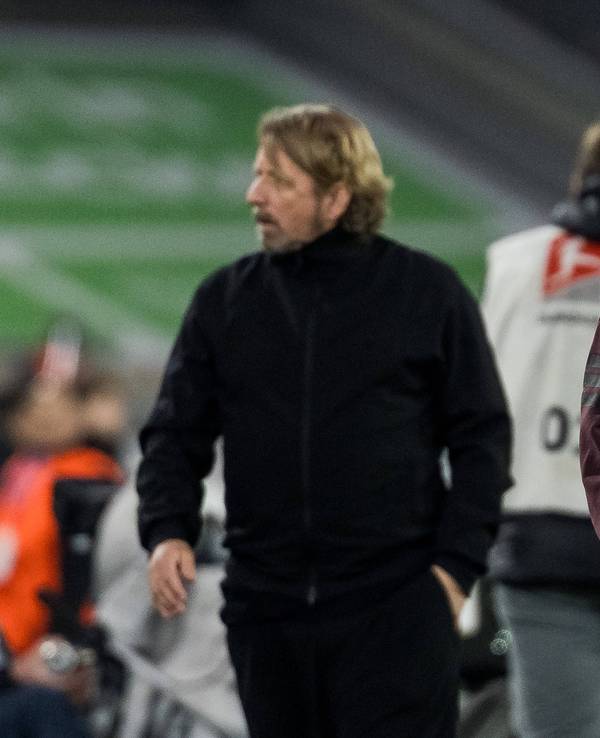 Markus Anfang schaut nachdenklich in die Luft, im Hintergrund geht Sven Mislintat.