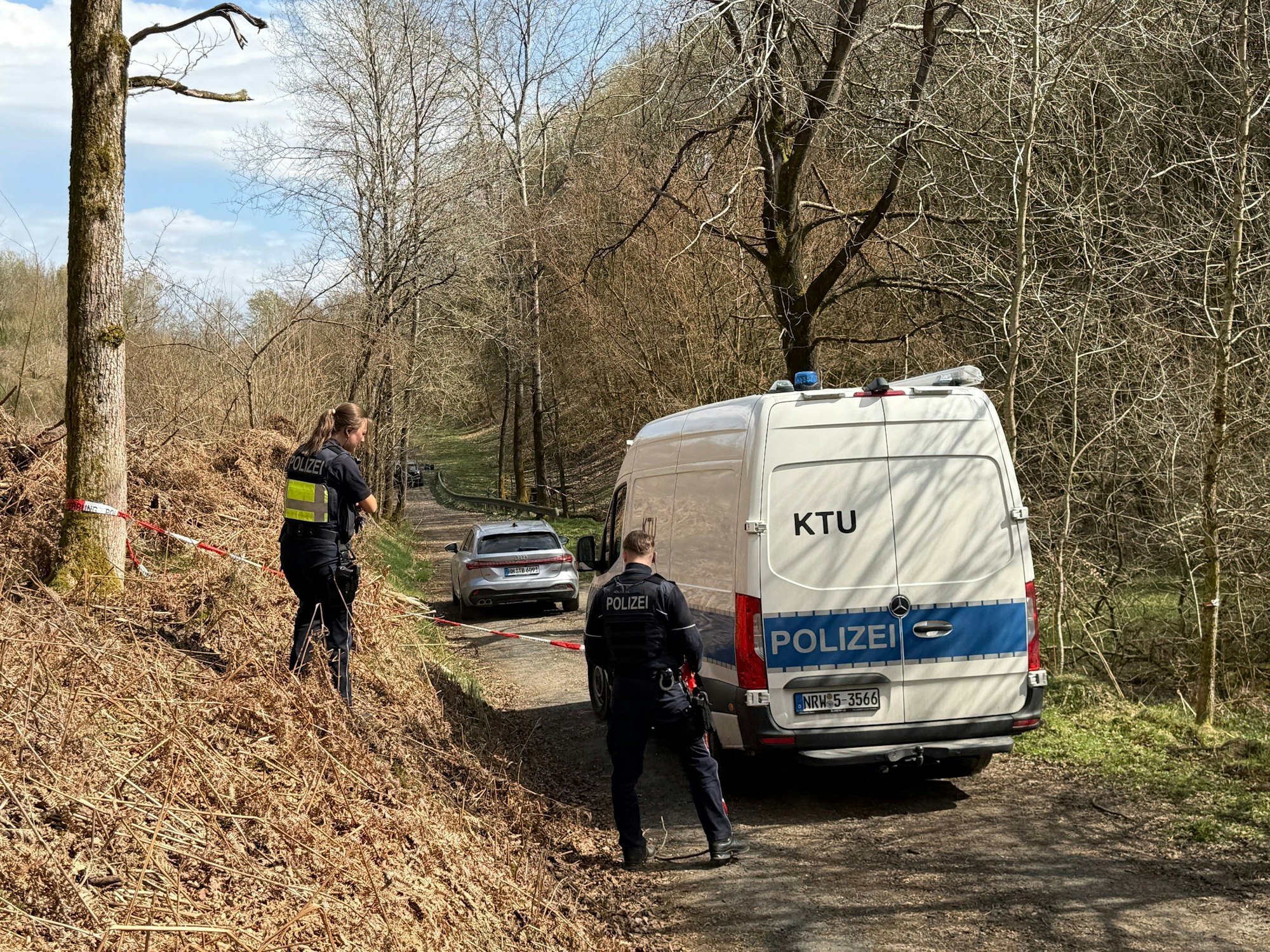 Kräfte der Polizei sind in einem mit Flatterband abgesperrten Bereich eines Waldes im Einsatz. Bei einer Müllsammelaktion wurde unweit der A4 ein menschlicher Kopf gefunden.