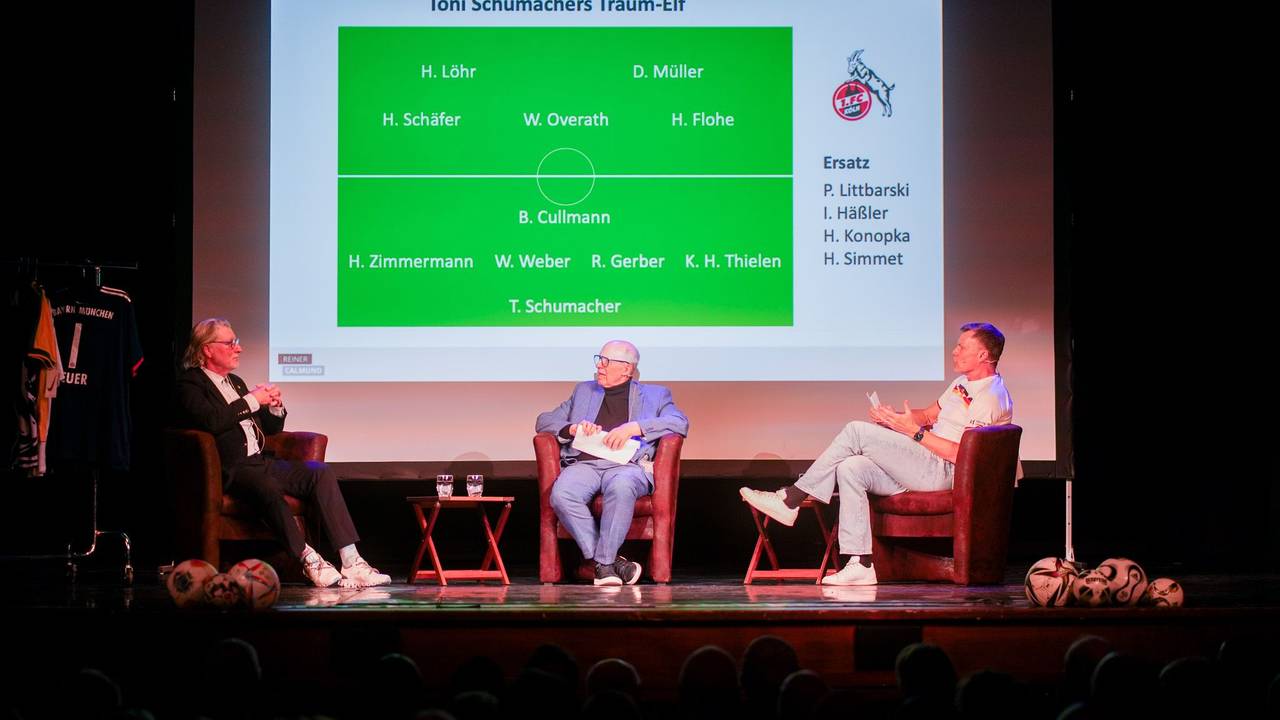 Toni Schumacher (l.) sitzt neben Reiner Calmund und Thomas Helmer (r.) auf der Bühne.
