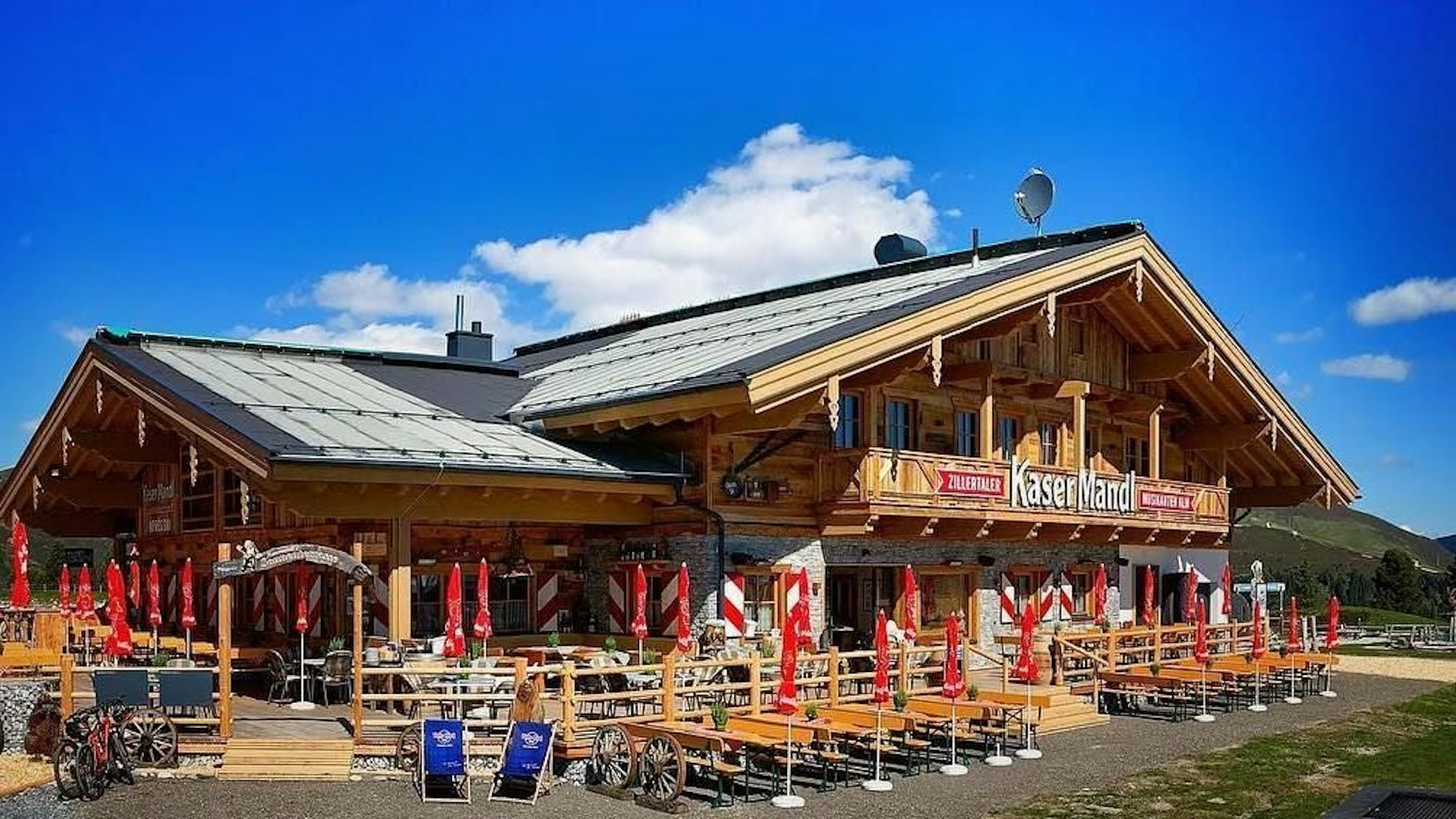 Rustikale, große Berghütte auh Holz mit Biergarten und roten Sonnenschirmen