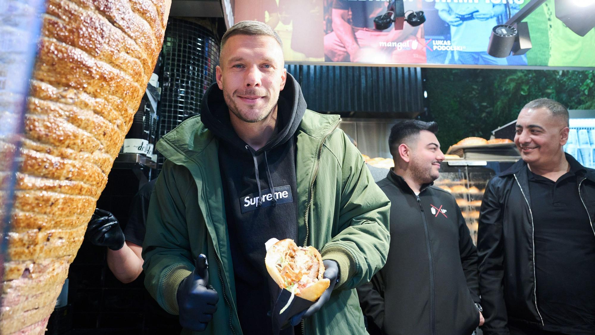 Lukas Podolski, ehemaliger Fußballprfoi und Unternehmer, zeigt seinen ersten Döner während der Eröffnung seines Döner-Imbiss.