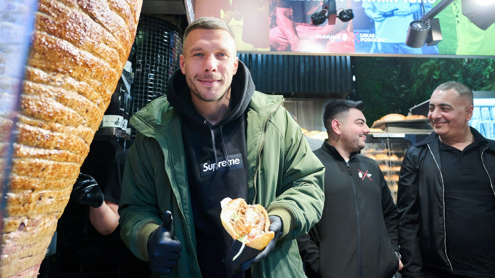 Lukas Podolski, ehemaliger Fußballprfoi und Unternehmer, zeigt seinen ersten Döner während der Eröffnung seines Döner-Imbiss.