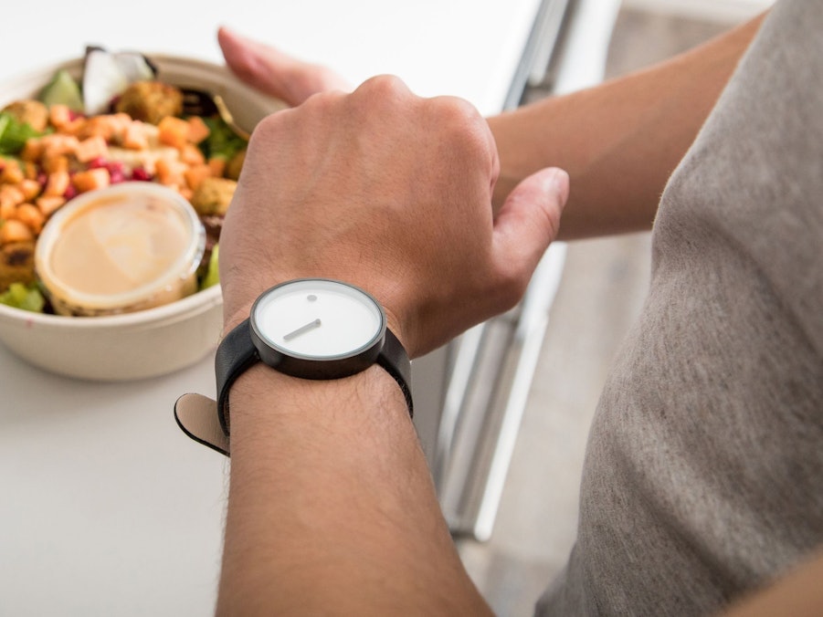 Mann mit einem Salat in der Hand schaut auf seine Armbanduhr