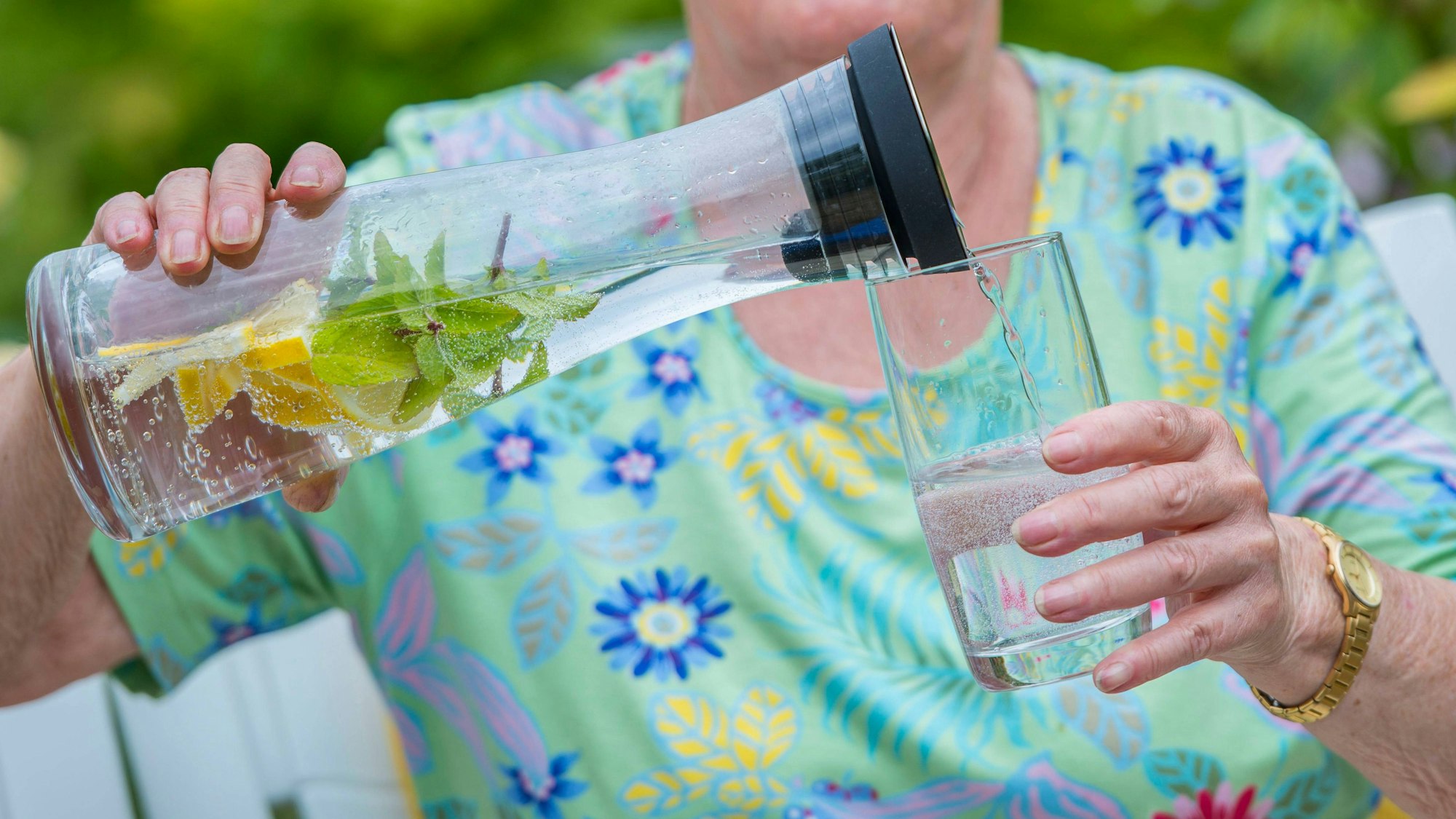 Aeltere Frau gießt Wasser in Glas