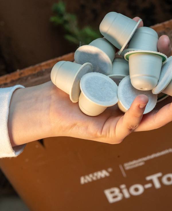 Frau hält kompostierbare Kaffeekapseln vor einer Bio-Mülltonne