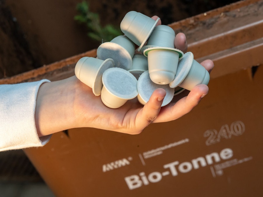 Frau hält kompostierbare Kaffeekapseln vor einer Bio-Mülltonne
