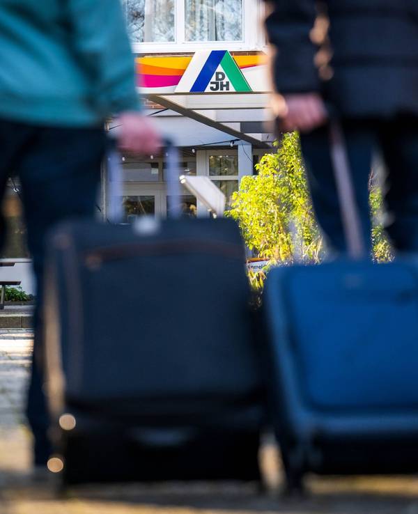 Gäste stehen mit Koffern und Taschen vor einer Jugendherberge