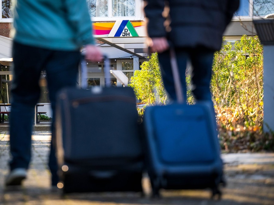 Gäste stehen mit Koffern und Taschen vor einer Jugendherberge