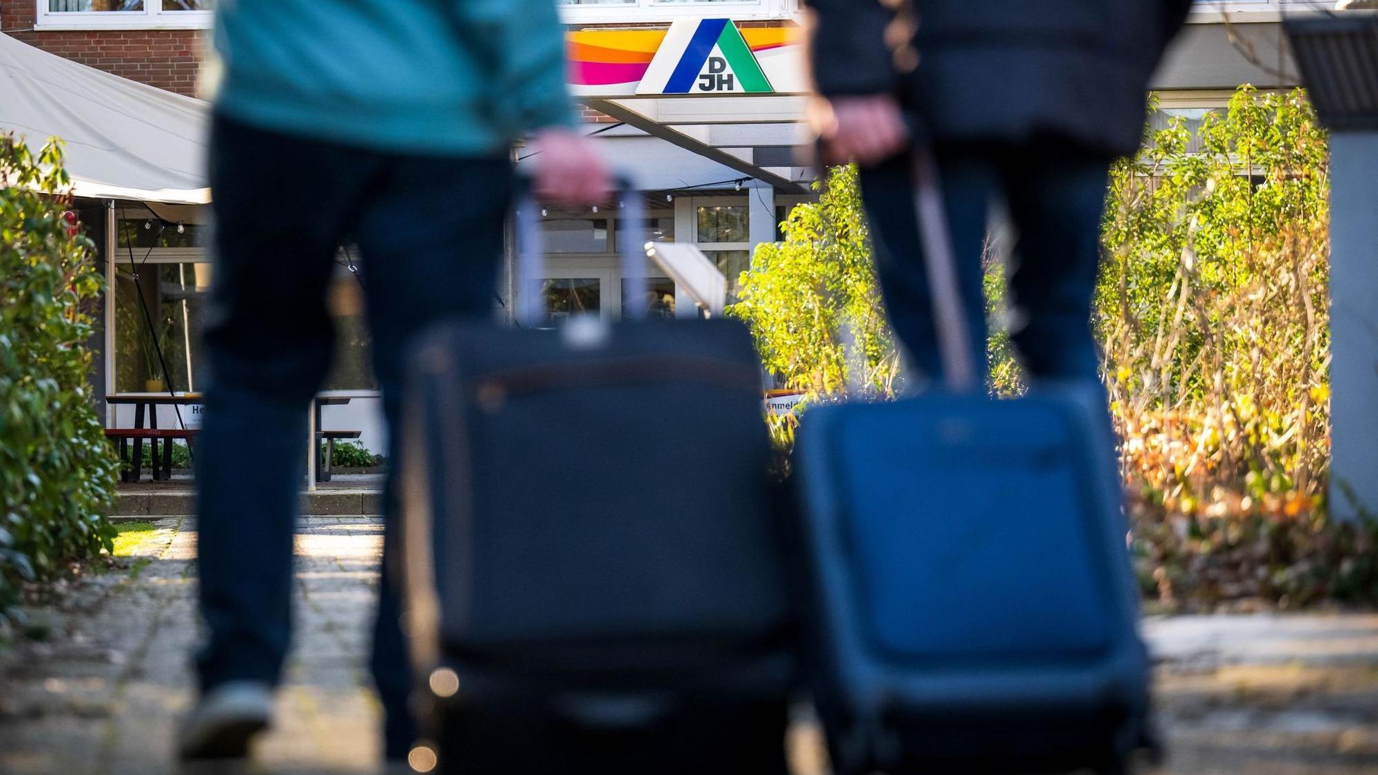 Gäste stehen mit Koffern und Taschen vor einer Jugendherberge