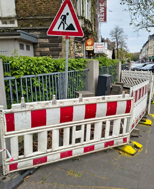 Die Dauerbaustelle in Köln-Riehl. Mit gelber Farbe hat ein Anwohner die Füße der Absperrungen markiert.