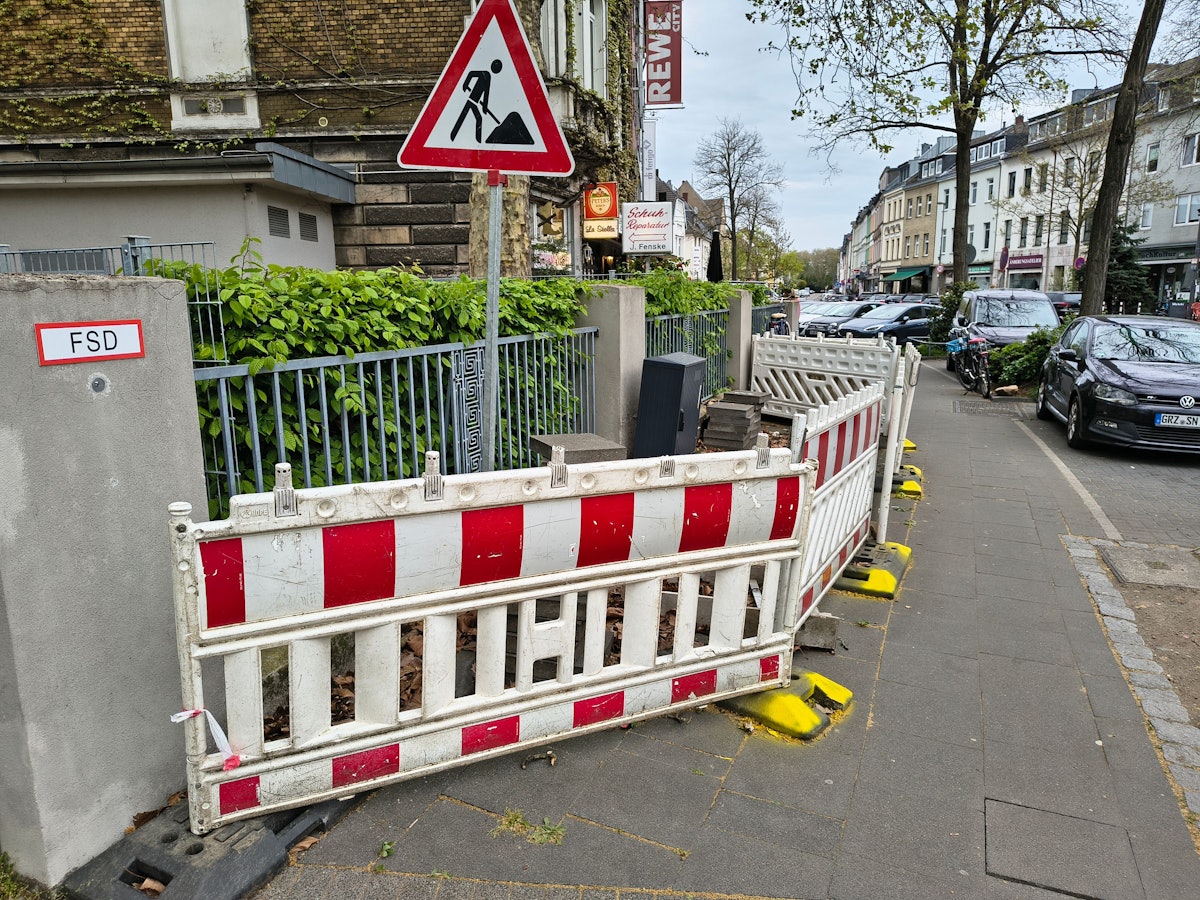 Die Dauerbaustelle in Köln-Riehl. Mit gelber Farbe hat ein Anwohner die Füße der Absperrungen markiert.
