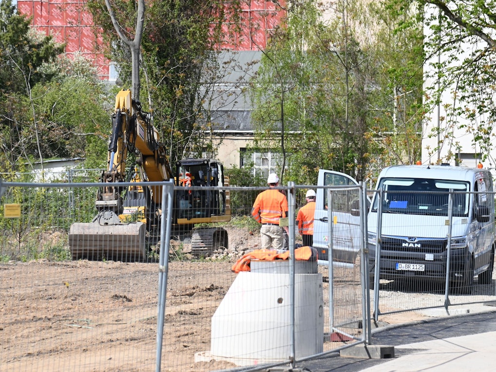 Zwei Männer stehen auf einer Baustelle vor einem Bagger.