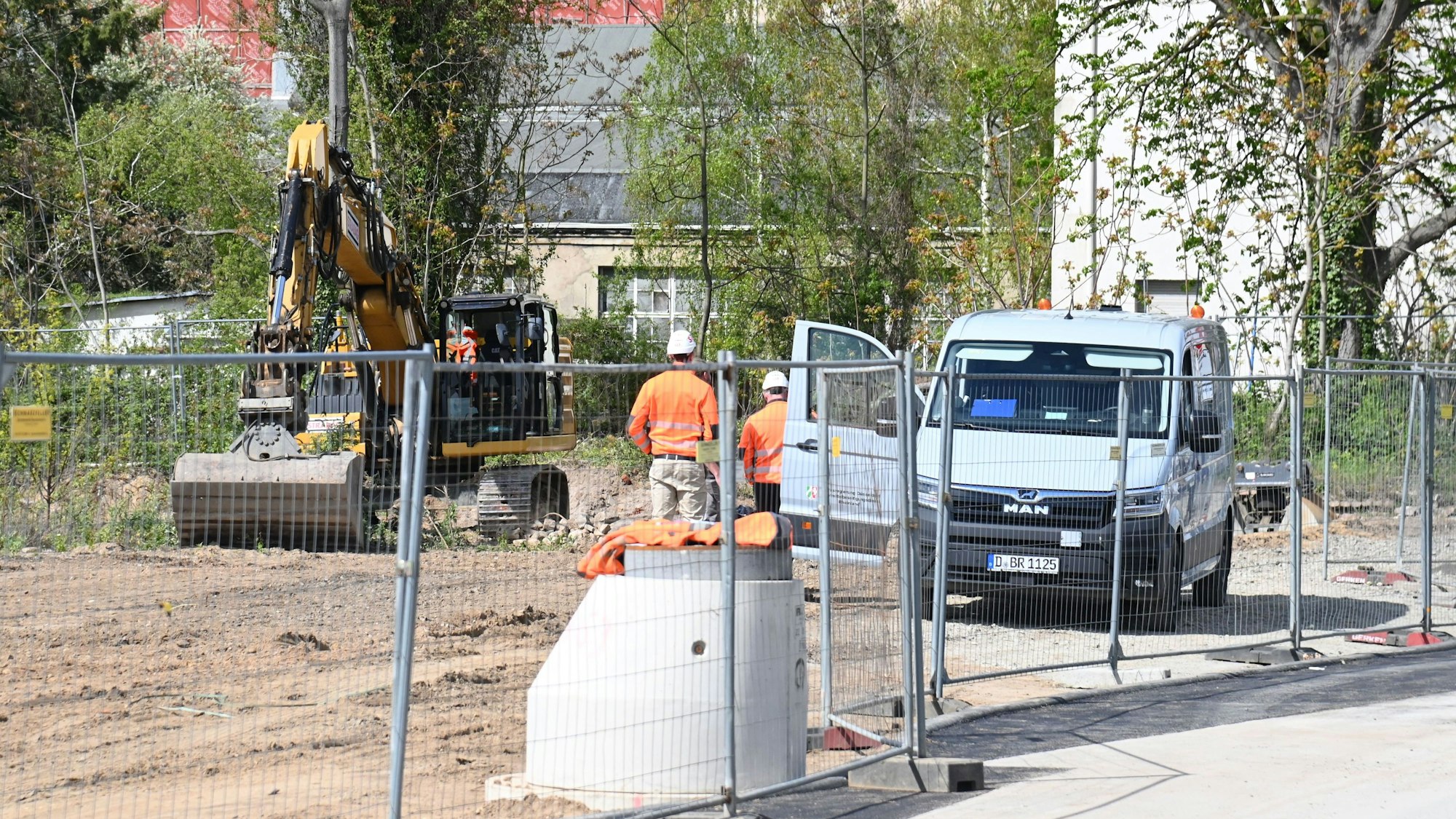 Zwei Männer stehen auf einer Baustelle vor einem Bagger.