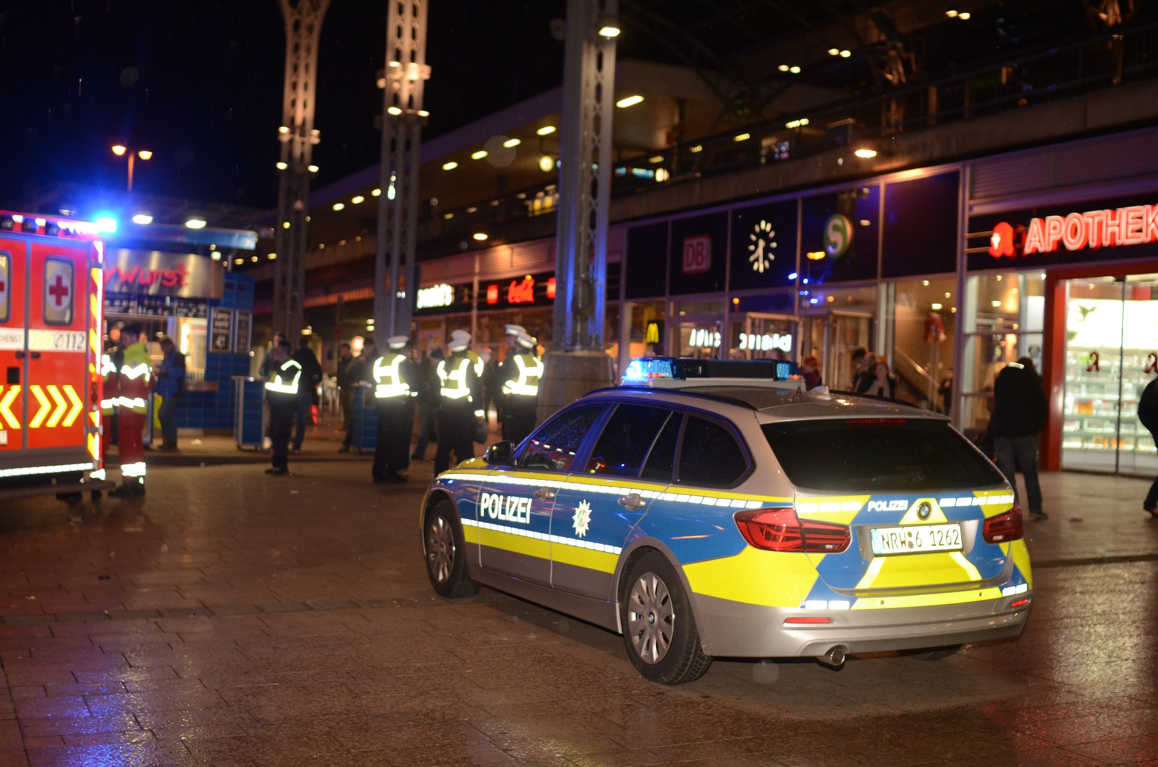 Polizeikräfte und ein Streifenwagen stehen nachts am Kölner Hauptbahnhof.