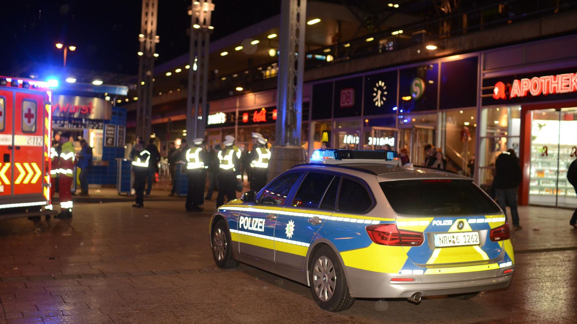 Polizeikräfte und ein Streifenwagen stehen nachts am Kölner Hauptbahnhof.