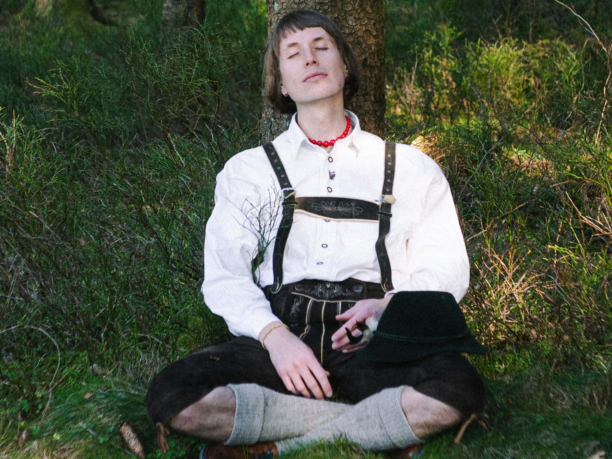 Ein Mnn in Lederhose lehnt an einem Baum.