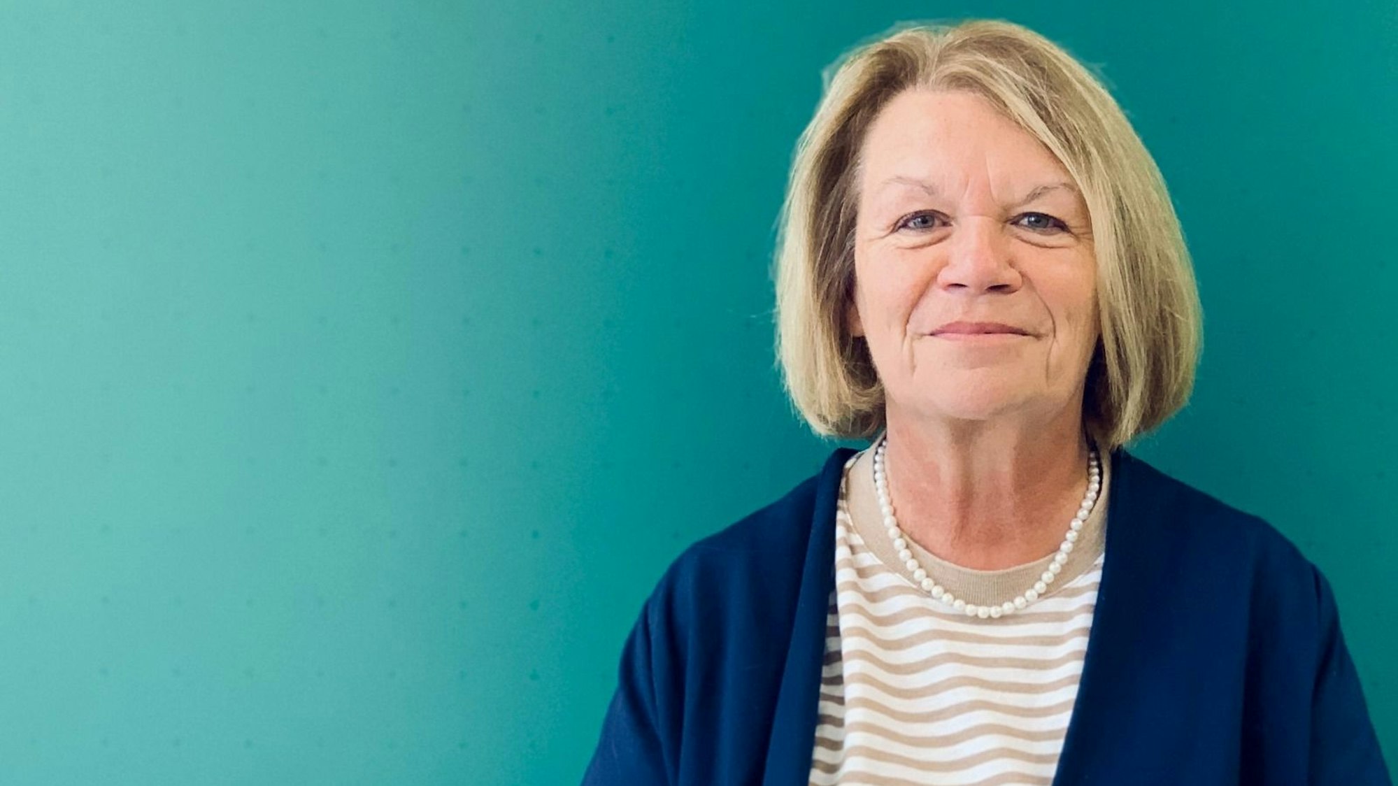 Eine Frau mit aschblondem Pagenschnitt, Perlenkette und Ringelshirt schaut freundlich in die Kamera