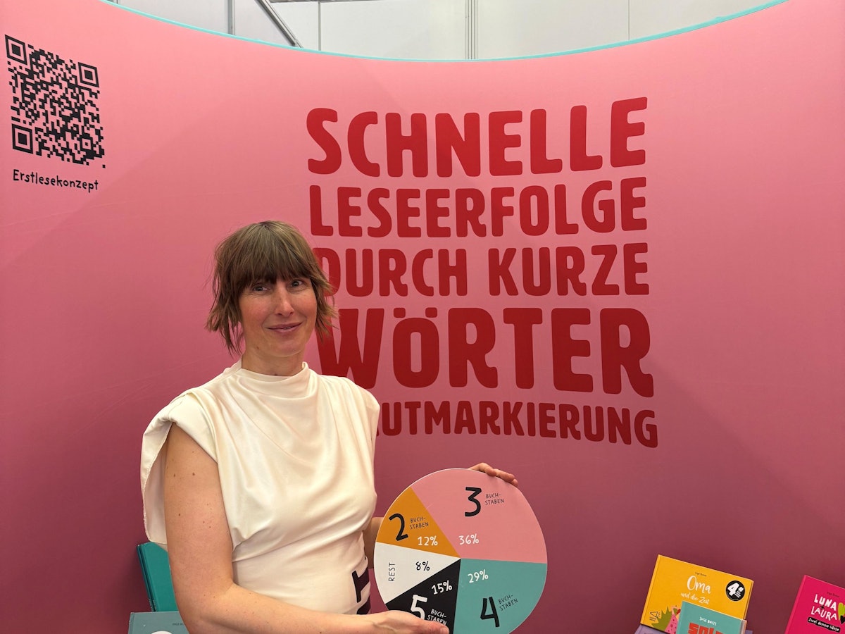 Eine Frau mit hochgesteckten Haaren in einem engen eierschalfarbenen Kleid hält eine Pappe mit einem Tortendiaframm vor einem roten Hintergrund in die Höhe.