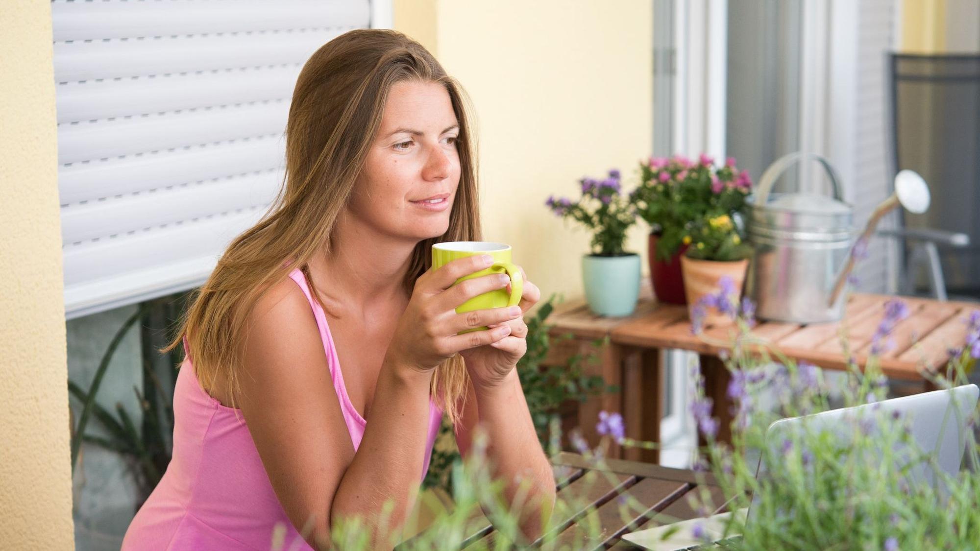 Frau sitzt auf einem Balkon und trinkt Kaffee