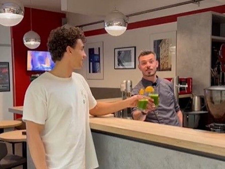 Zwei Männer stoßen an der Bar im Sportcenter Katz mit einem grünen Detox-Saft an.