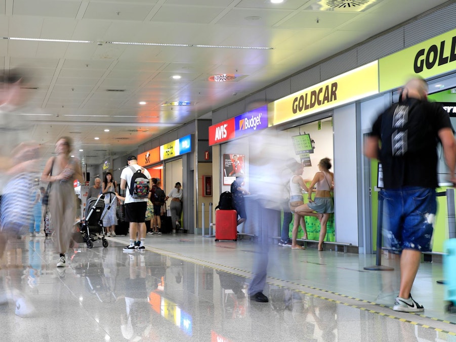 Menschen gehen an Mietwagen-Firmen vorbei