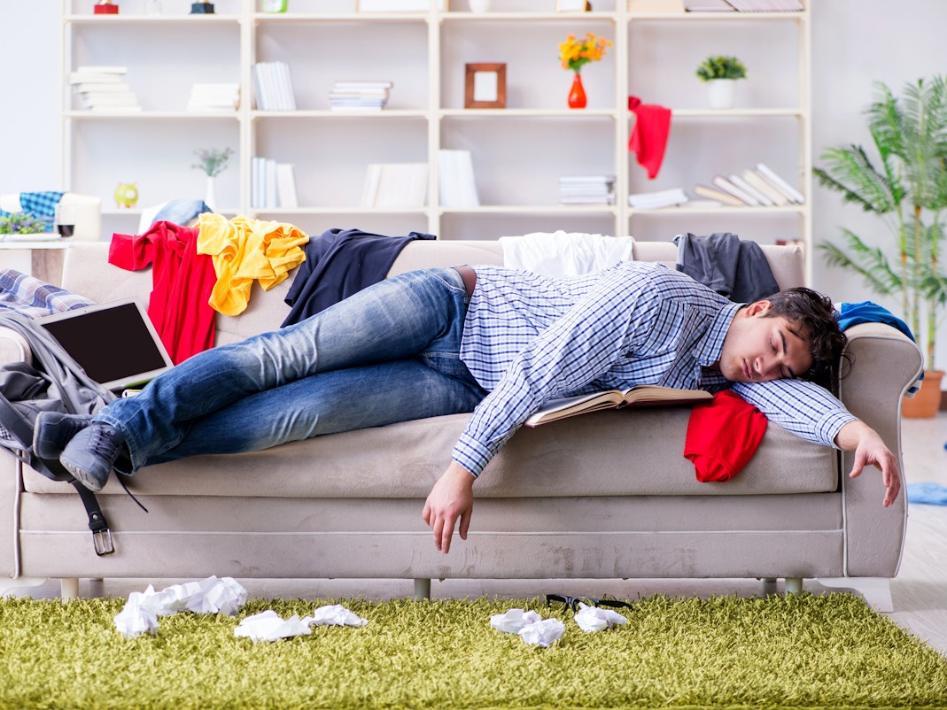 Ein pubertierender junger Mann hängt auf der Couch mittem im Chaos seines Kinderzimmers