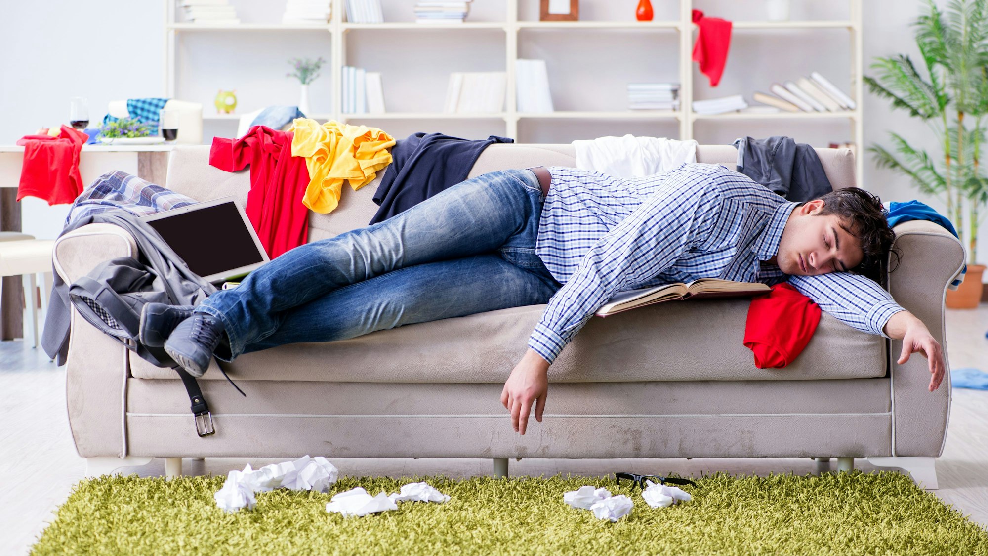 Ein pubertierender junger Mann hängt auf der Couch mittem im Chaos seines Kinderzimmers