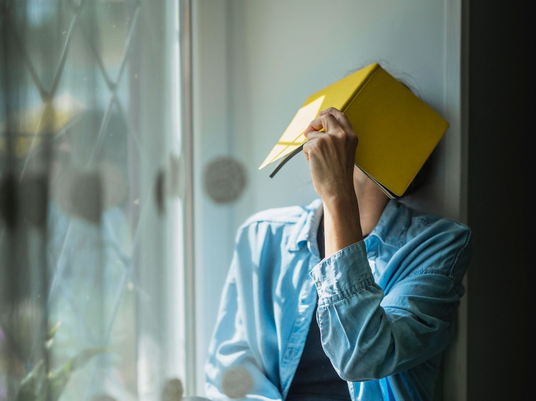 Eine Frau verbirgt ihr Gesicht hinter einem Notizheft