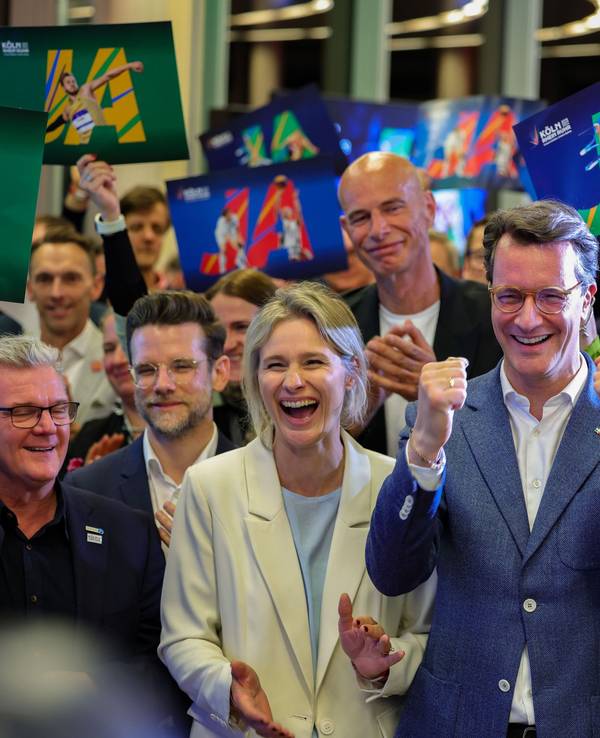 NRW-Ministerpräsident Hendrik Wüst (CDU, Mitte) und Kölns OB Torsten Burmester (r.) jubeln nach der erfolgreichen Abstimmung um die Olympischen Spiele in Nordrhein-Westfalen.