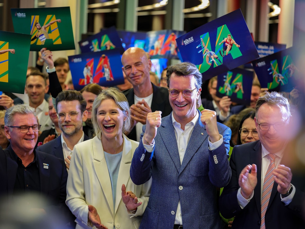 NRW-Ministerpräsident Hendrik Wüst (CDU, Mitte) und Kölns OB Torsten Burmester (r.) jubeln nach der erfolgreichen Abstimmung um die Olympischen Spiele in Nordrhein-Westfalen.