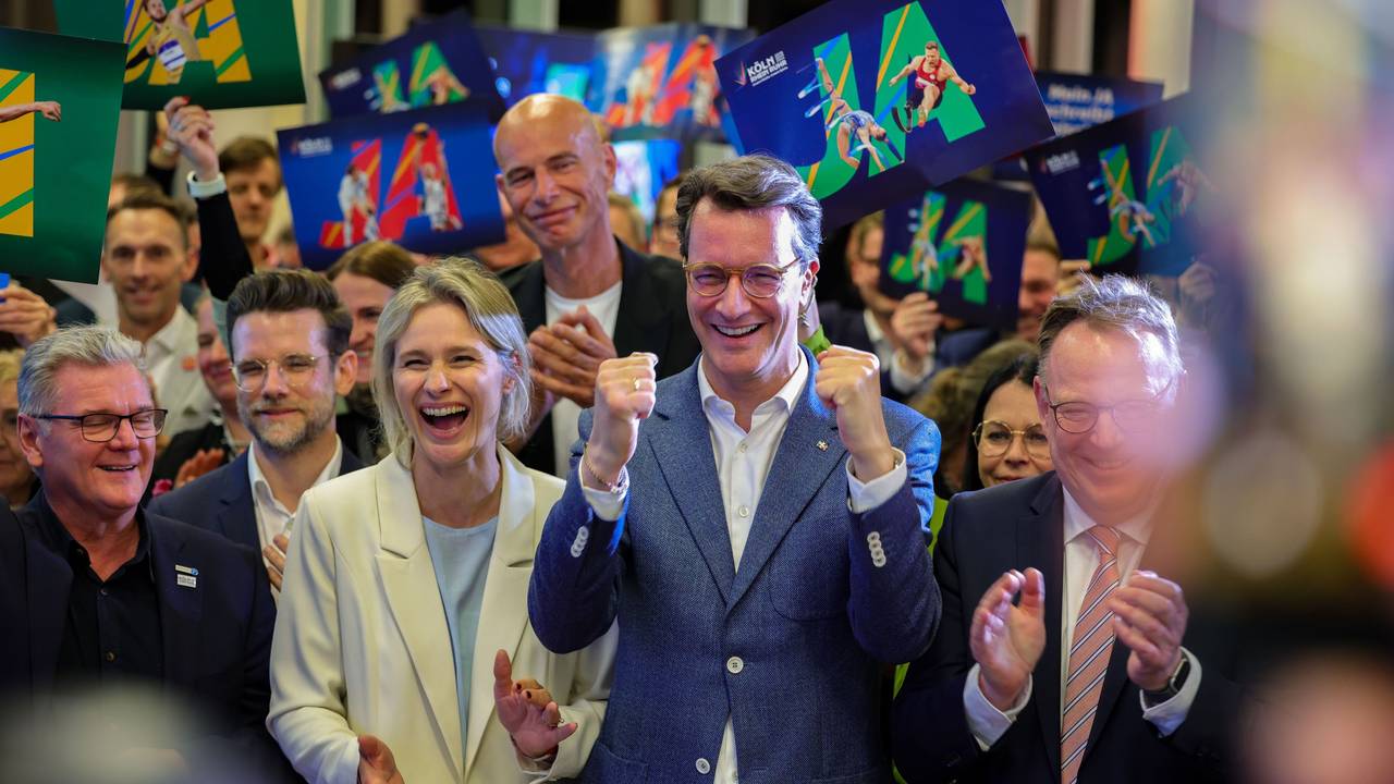 NRW-Ministerpräsident Hendrik Wüst (CDU, Mitte) und Kölns OB Torsten Burmester (r.) jubeln nach der erfolgreichen Abstimmung um die Olympischen Spiele in Nordrhein-Westfalen.